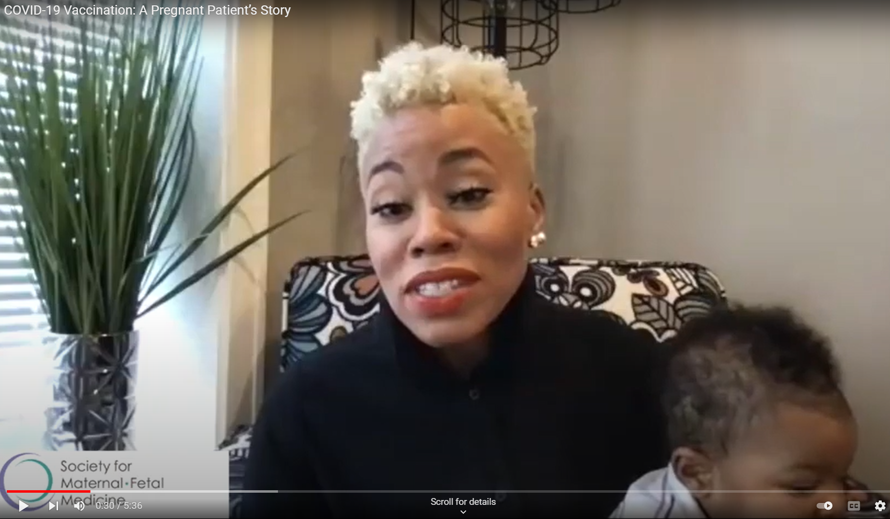 A Black woman holds her baby and speaks into the camera. 