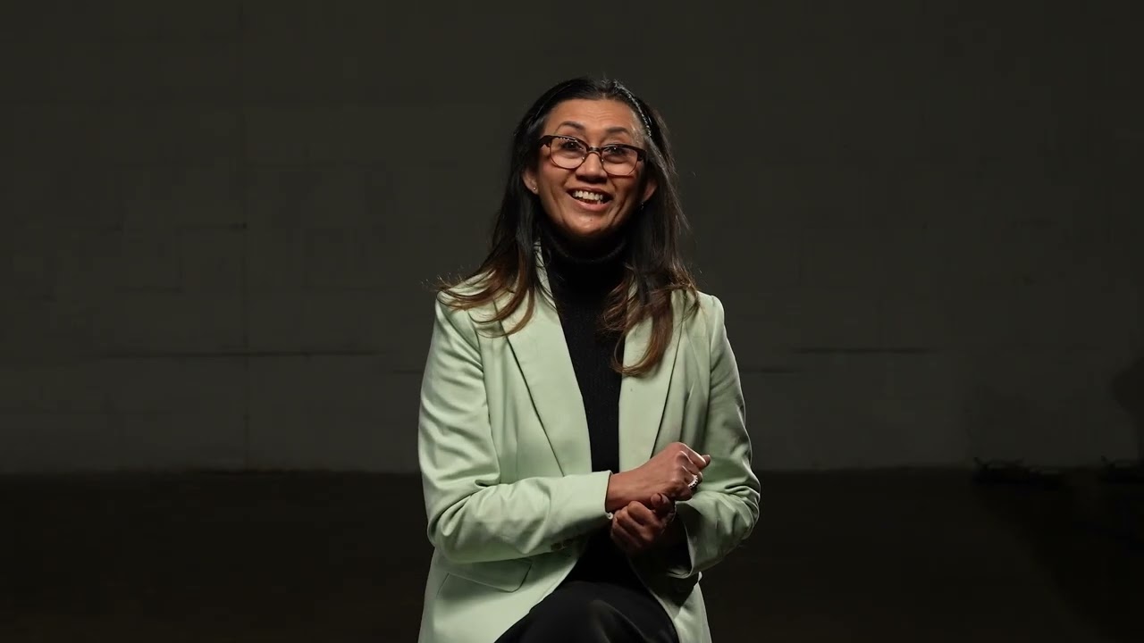 A woman wearing glasses and a green blazer is speaking. 