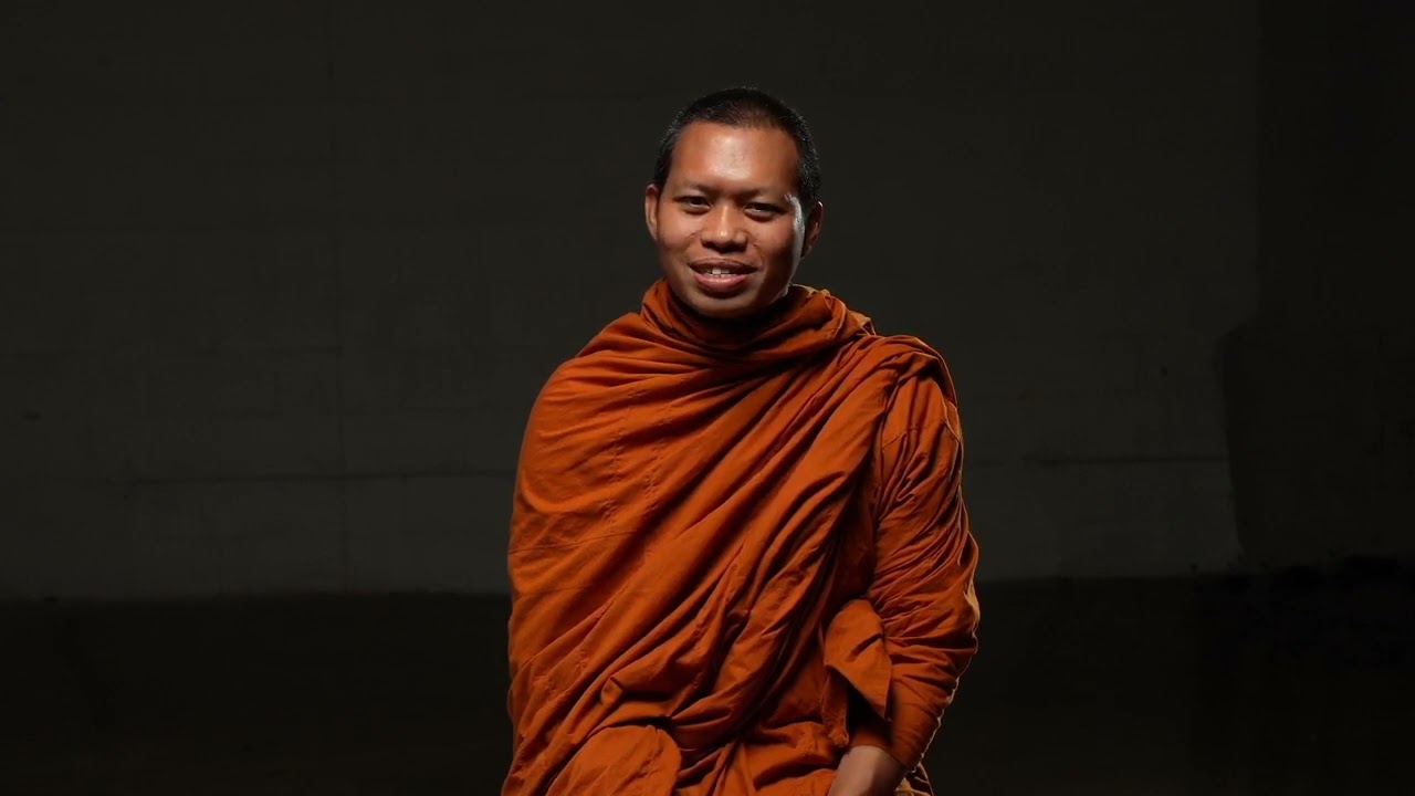 An Asian man wearing orange robes is speaking. 