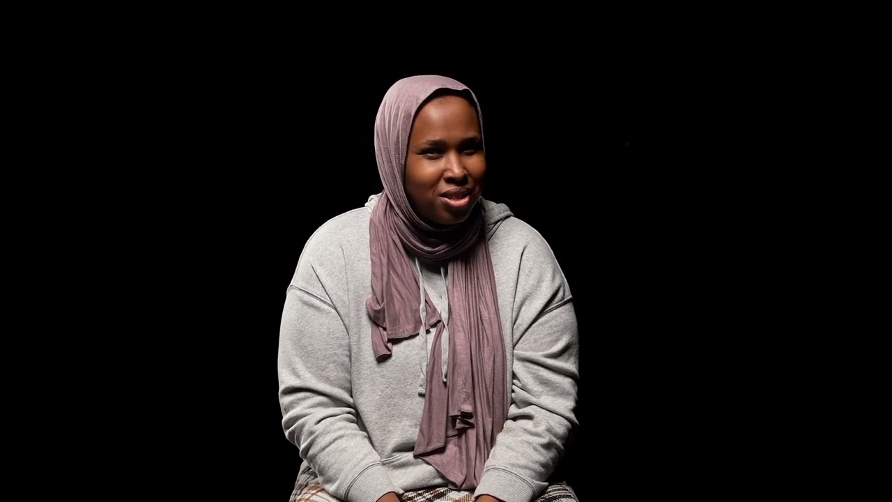 A Black woman wearing a sweater and headscarf is speaking. 