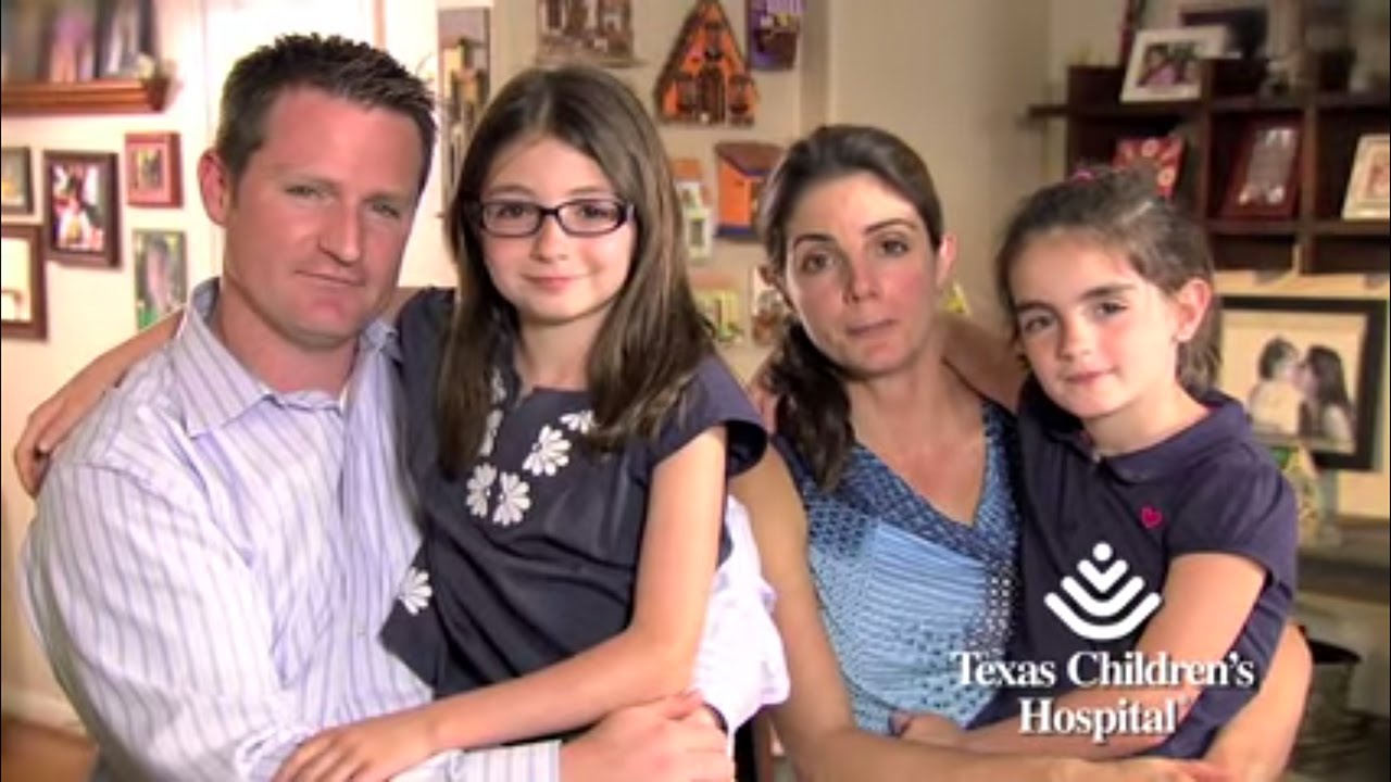 Two young daughters are sitting on the laps of their mother and father inside their home. The Texas Children's Hospital logo is on the bottom right corner.