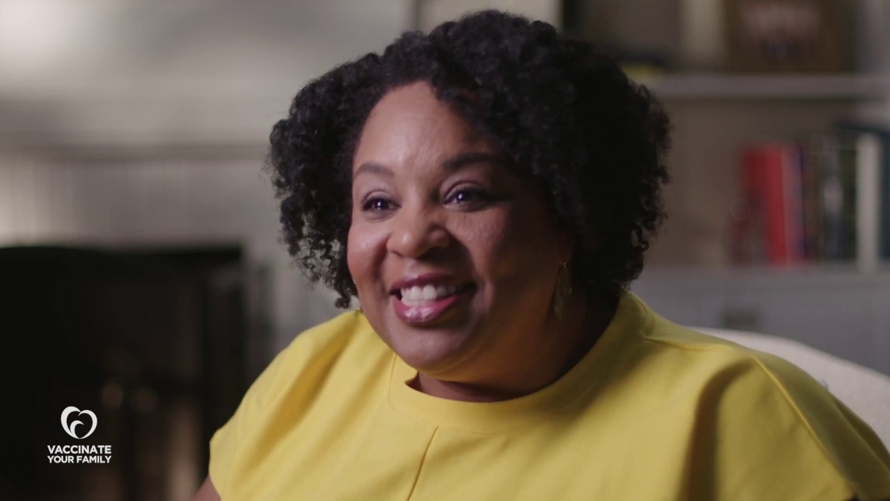 Tamika Felder, a Black woman, smiles and speaks from a living room. 