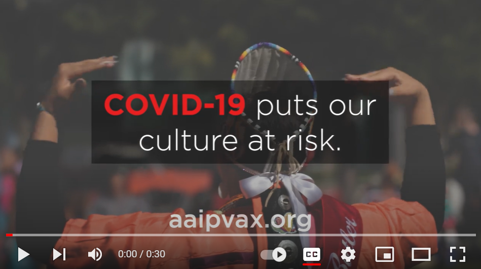 Still from a video shows the back of an Indigenous person wearing a headdress 