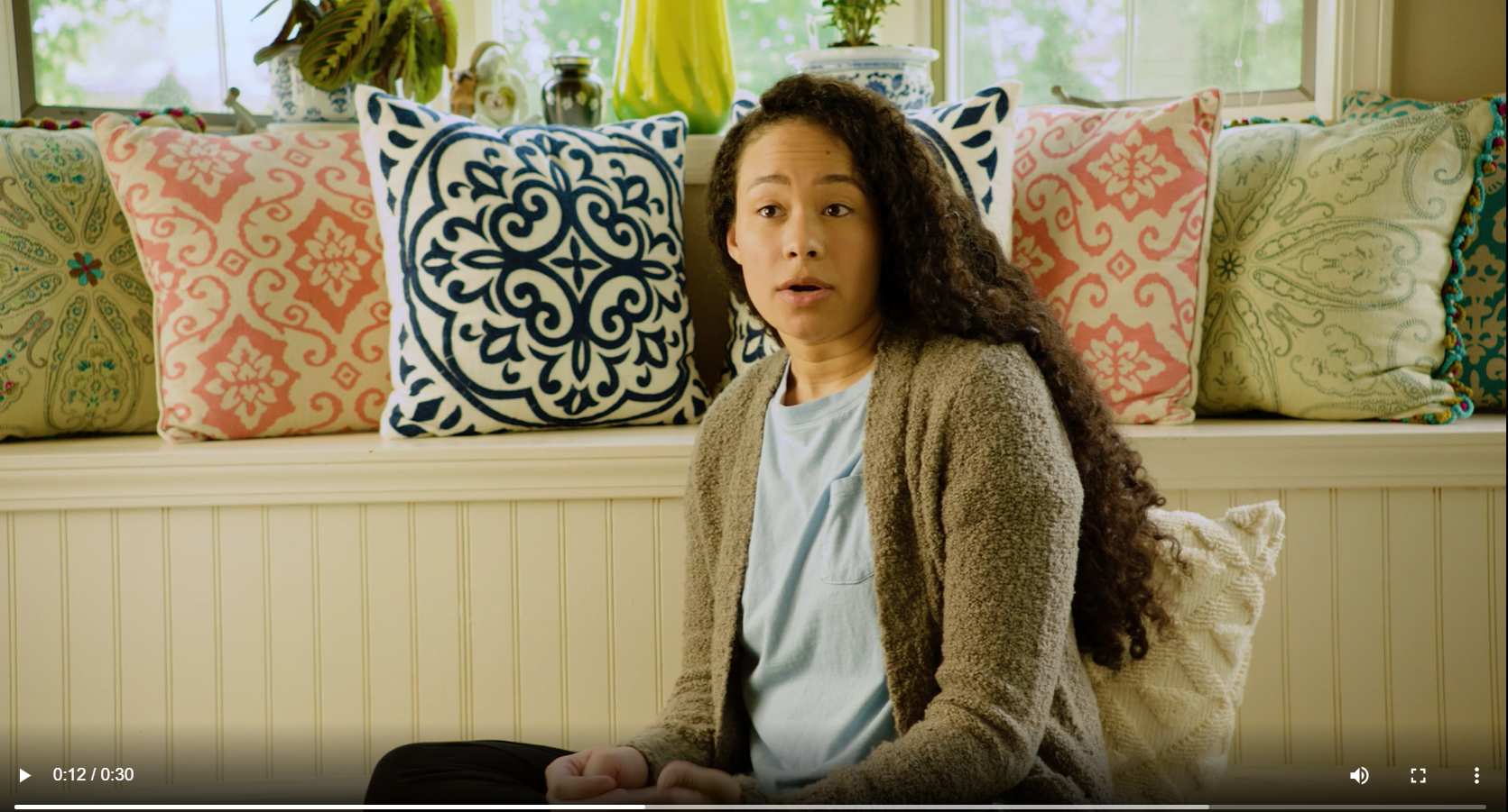 a Black woman wearing a light blue t-shirt and a green sweater speaks 