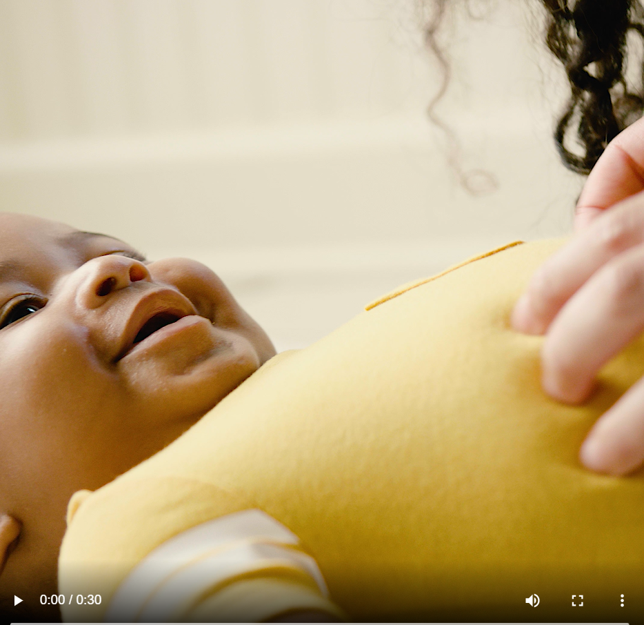 An African American baby smiles while his mom rubs his stomache