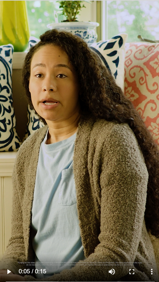 a Black woman wearing a light blue t-shirt and a green sweater speaks 