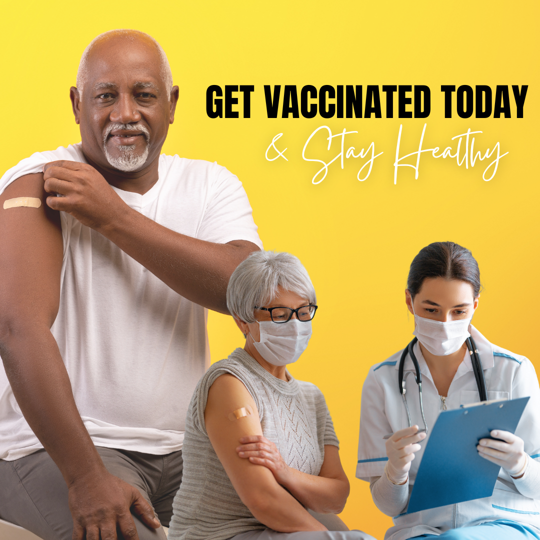 An older Black man rolls up his sleeve to show an adhesive bandage on his arm. In the corner, an older woman talks with a healthcare provider. She has an adhesive bandage on her arm. 