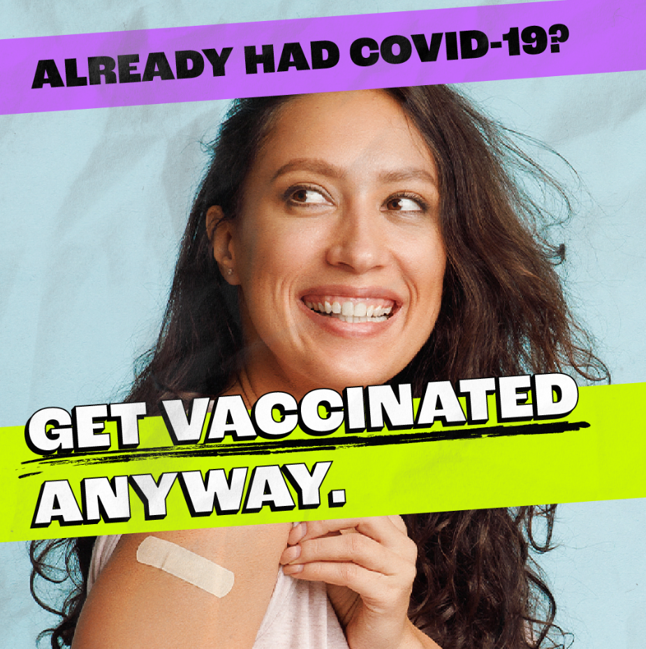 A person smiles while proudly showing a Band-Aid on her arm after getting vaccinated.