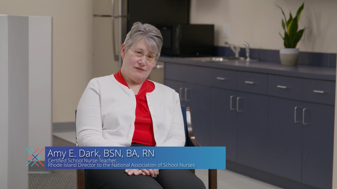 Amy E. Dark, BSN, BA, RN, a white female certified school Nurse-Teacher with short grey hair and glasses is discussing school vaccine mandates and the importance of the HPV vaccine regardless of school requirements.