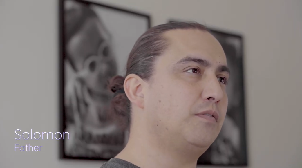 Indigenous father, Solomon, with dark brown hair, is in his home giving a testimonial.