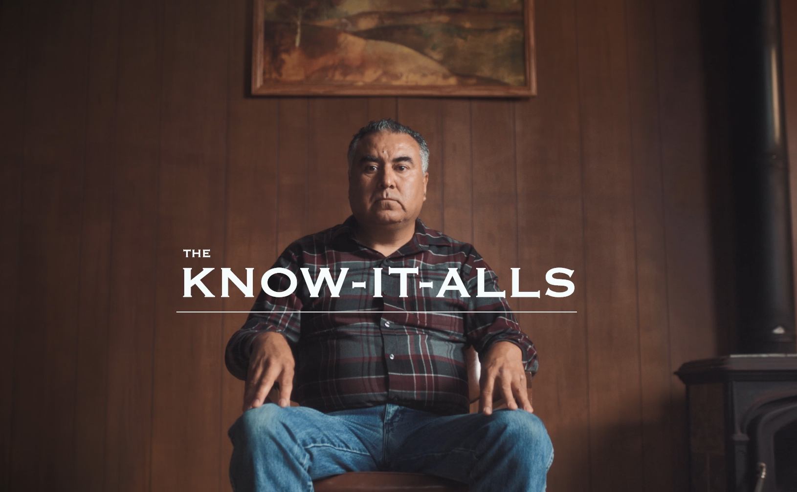 A Hispanic/Latino man sits in a chair in a wood-paneled room. The title reads, "The Know-It-Alls."
