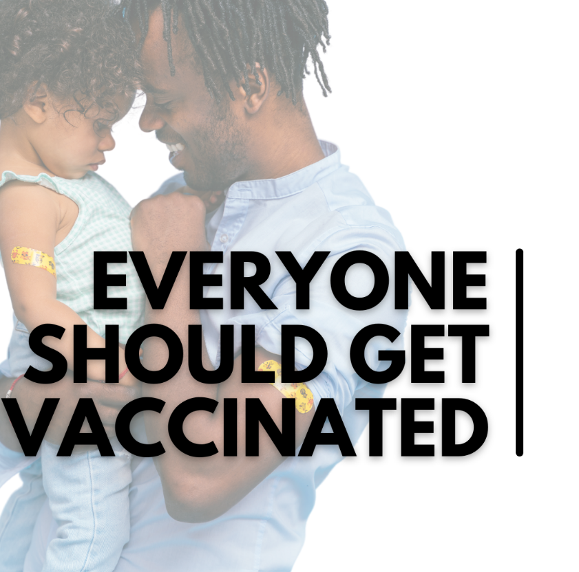 A Black man smiles and holds a child, who has a bandaid on their arm. 