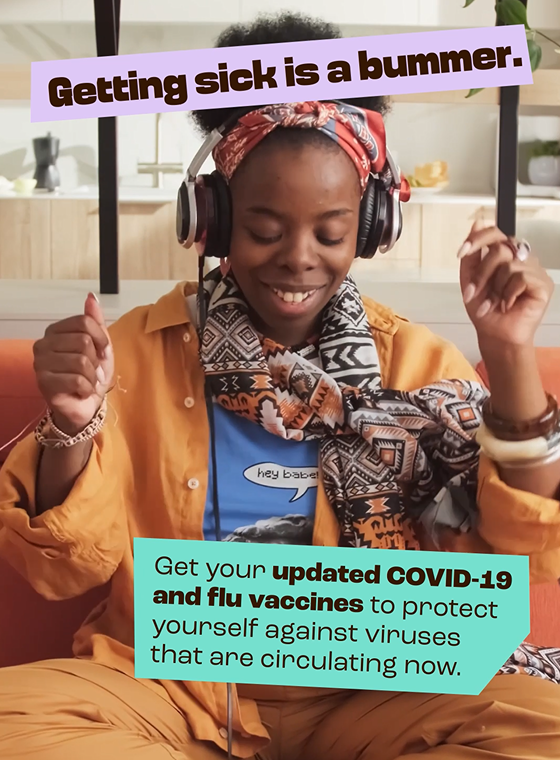 Black woman smiles broadly while dancing and listening to music on their phone.