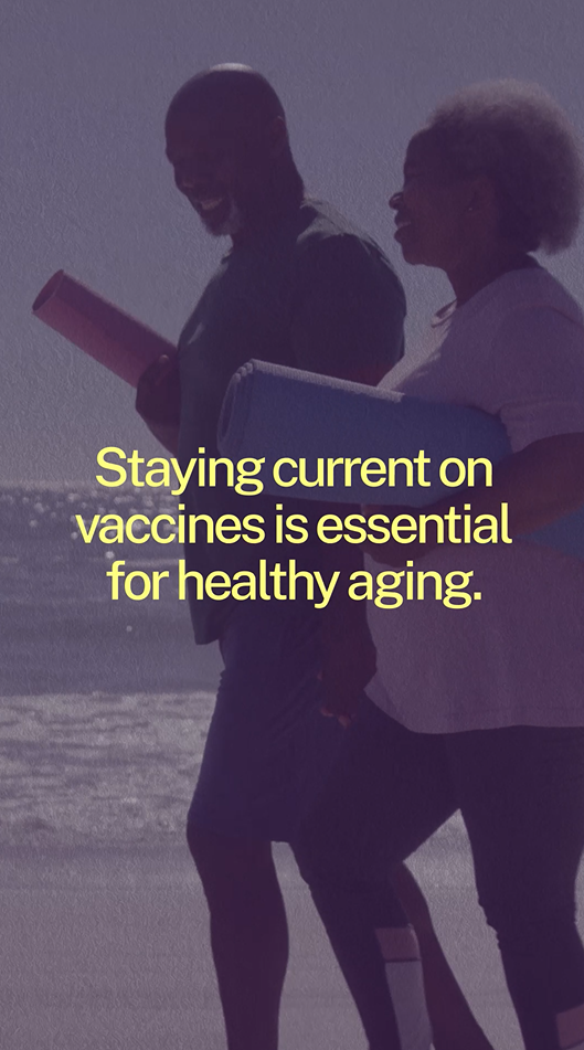 An older Black man and woman smile and walk on the beach with yoga mats in their hands.