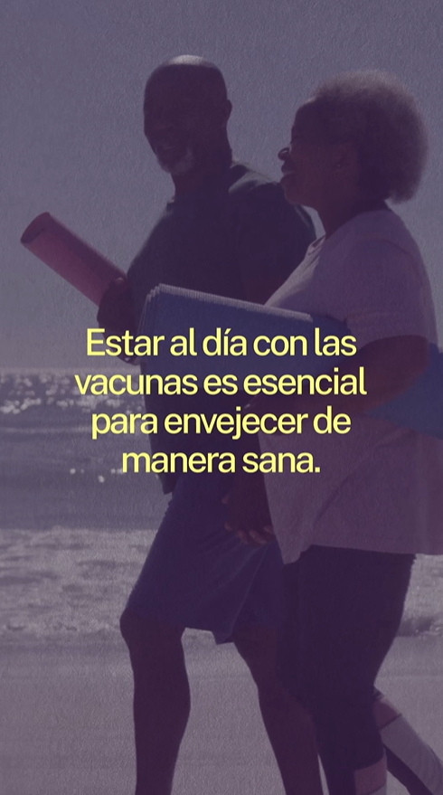 An older Black man and woman smile and walk on the beach with yoga mats in their hands.