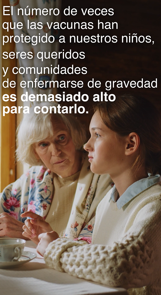 Video still shows a girl and her grandmother, sitting at a table together, looking out the sunny window, and talking over a cup of tea. 
