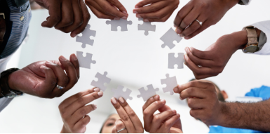 Graphic includes multiple hands holding white puzzle pieces.