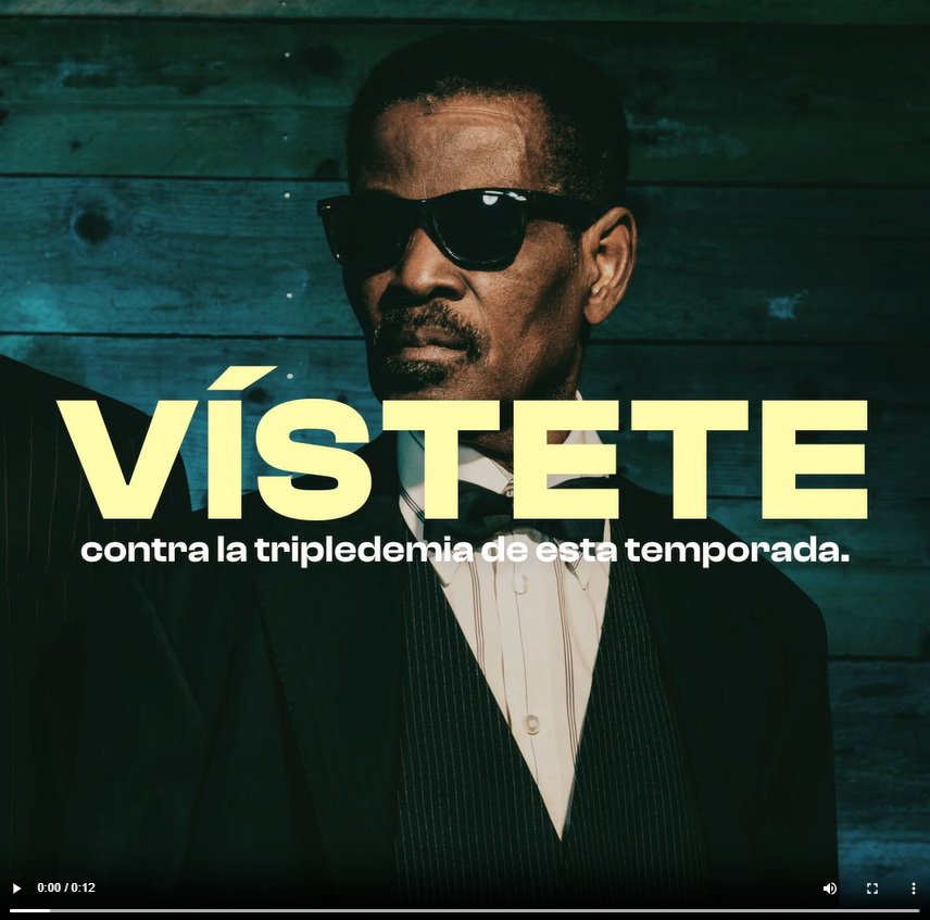 A Black man wearing sunglasses and a suit poses 